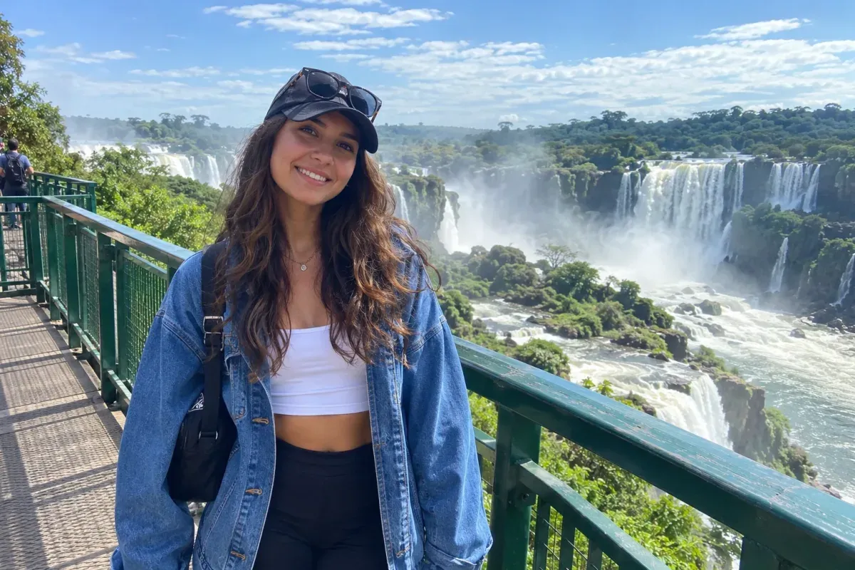 Jovem de boné, jaqueta jeans e mochila na passarela das Cataratas do Iguaçu, em foto na altura dos olhos