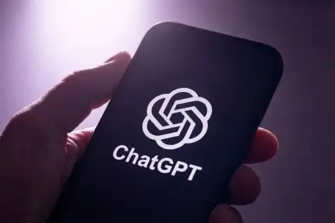 Mão segurando um celular com o logotipo do ChatGPT na tela em um ambiente escuro com luz roxa