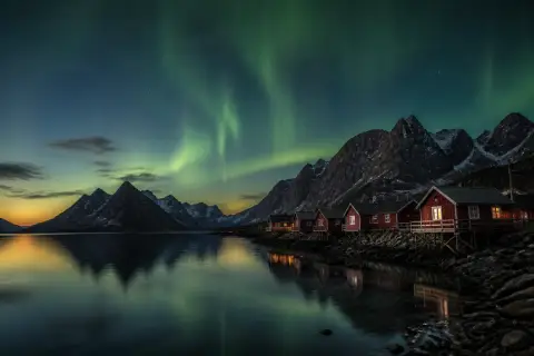 Casas vermelhas de madeira à beira de um fiorde na Noruega, com montanhas e aurora boreal no céu ao entardecer
