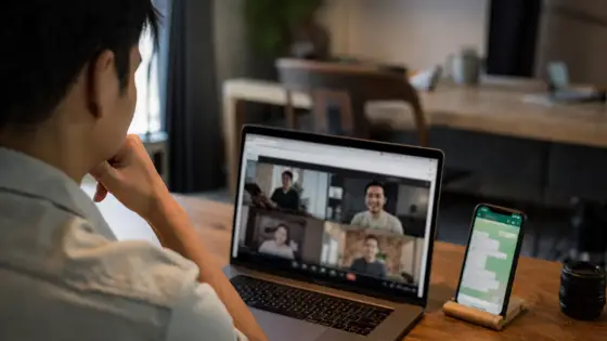 Pessoa em uma videochamada no navegador do notebook, com um celular com WhatsApp ao lado