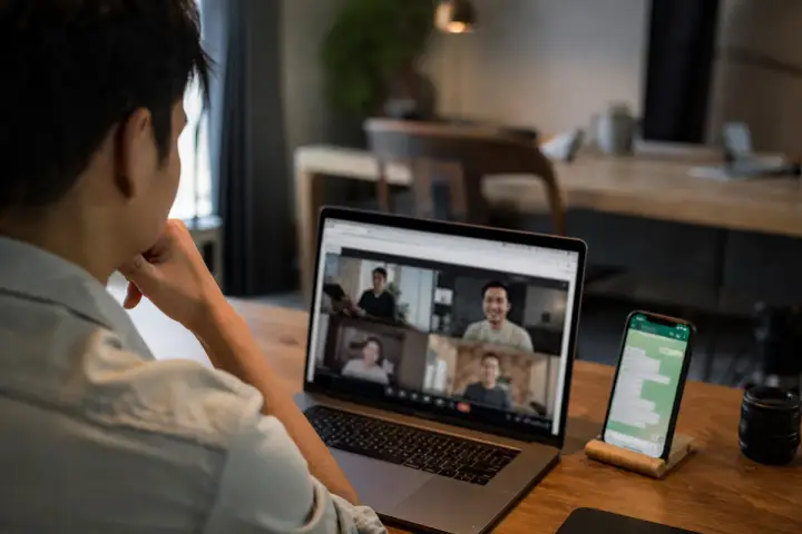 Pessoa em uma videochamada no navegador do notebook, com um celular com WhatsApp ao lado